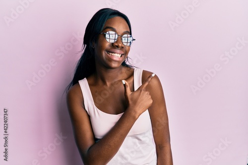Young african american woman wearing casual clothes and glasses smiling cheerful pointing with hand and finger up to the side