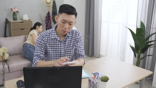 asian mother carrying a child is coming over to look at the useful banking loan information her husband just found out with a calculator.