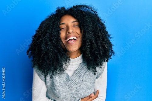 African american woman with afro hair wearing casual winter sweater smiling and laughing hard out loud because funny crazy joke with hands on body.