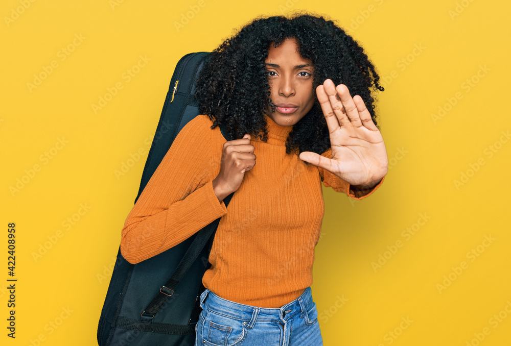 Young african american girl wearing guitar case with open hand doing stop sign with serious and confident expression, defense gesture Young african american girl wearing guitar case with open hand doing stop sign with serious and confident expression, defense gesture