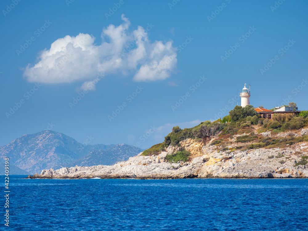 view to rock cliff at sea with alone lighthouse under blue sky with white cloud