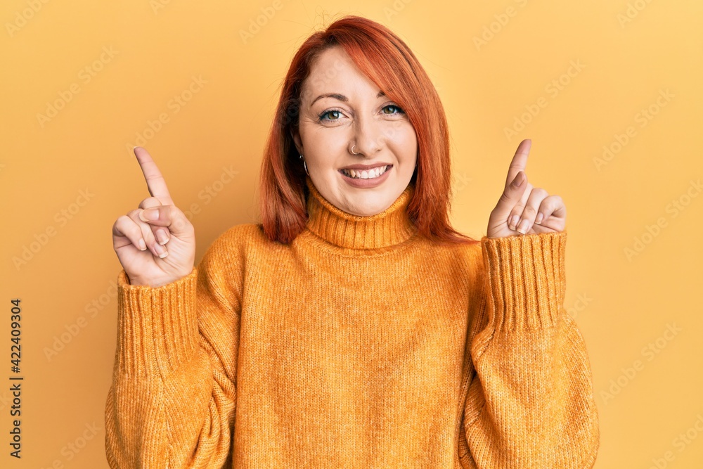 Beautiful redhead woman wearing casual winter sweater over yellow background smiling confident pointing with fingers to different directions. copy space for advertisement