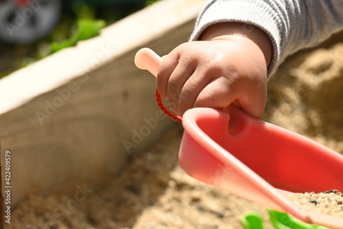 Close-up at a child hand playing at the sand pit holding a plastic shovel