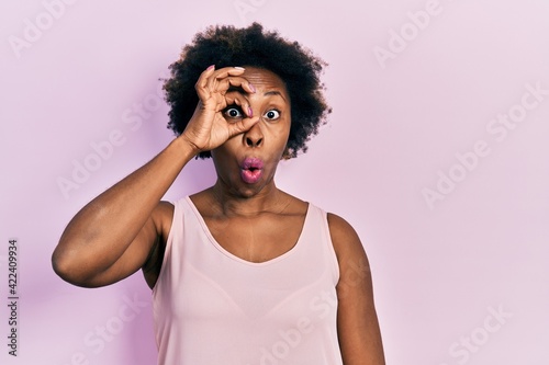 Young african american woman wearing casual sleeveless t shirt doing ok gesture shocked with surprised face, eye looking through fingers. unbelieving expression.