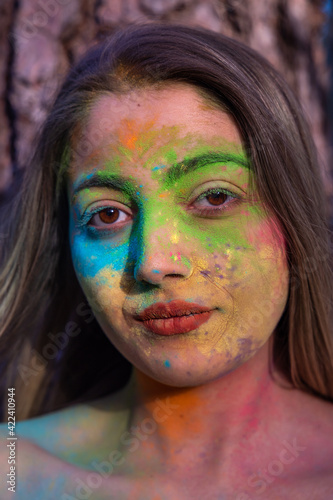 Young attractive woman at the Holi color festival of paints in park. Having fun outdoors. Multi Colored powder colors the face. Close Up portrait, people. Copy Space.