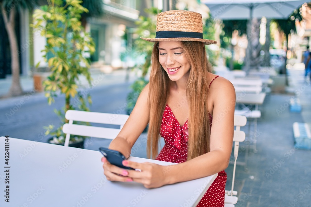 Fototapeta premium Young caucasian tourist girl smiling happy using smartphone at coffee shop terrace