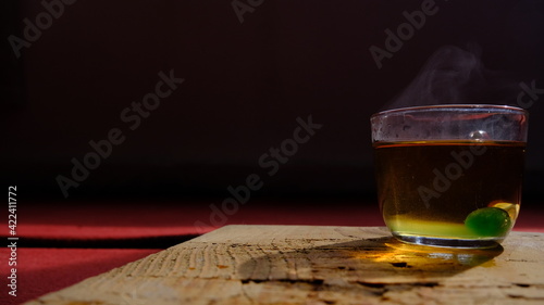 Isolated linden tea cup made of glass and there is green mentholated sweat and candy. Fully linden tea filled glass pot existing on wooden plate and red carpet. photo