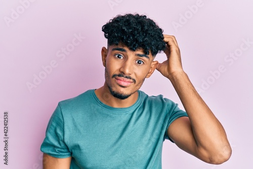 Young arab handsome man wearing casual clothes confuse and wonder about question. uncertain with doubt  thinking with hand on head. pensive concept.