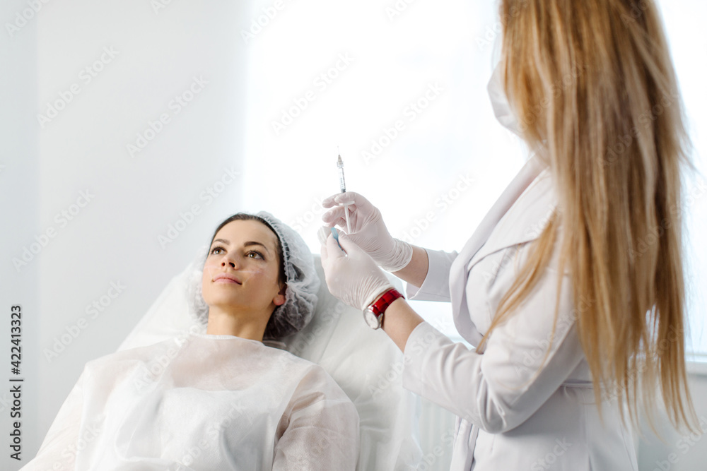 Attractive young woman is getting a rejuvenating facial injections. She is sitting calmly at clinic. The expert beautician is filling female wrinkles by hyaluronic acid. High quality photo Attractive young woman is getting a rejuvenating facial injections. She is sitting calmly at clinic. The expert beautician is filling female wrinkles by hyaluronic acid. High quality photo