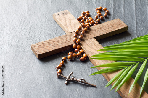 Wooden cross, rosary and palm on black marble background, palm sunday concept photo