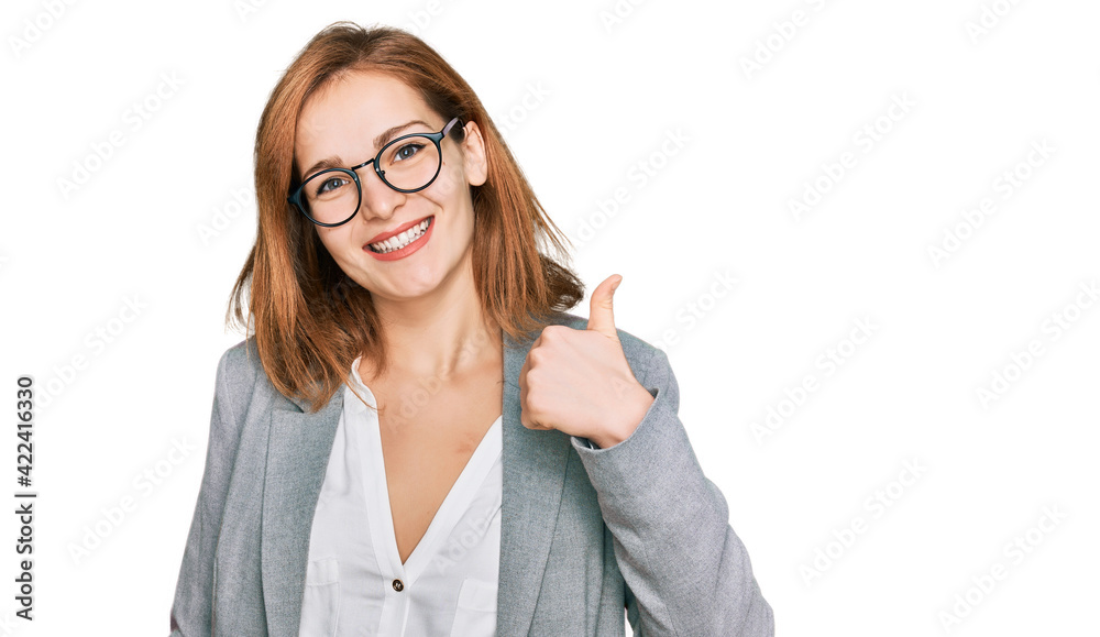 Young caucasian woman wearing business style and glasses doing happy thumbs up gesture with hand. approving expression looking at the camera showing success. Young caucasian woman wearing business style and glasses doing happy thumbs up gesture with hand. approving expression looking at the camera showing success.