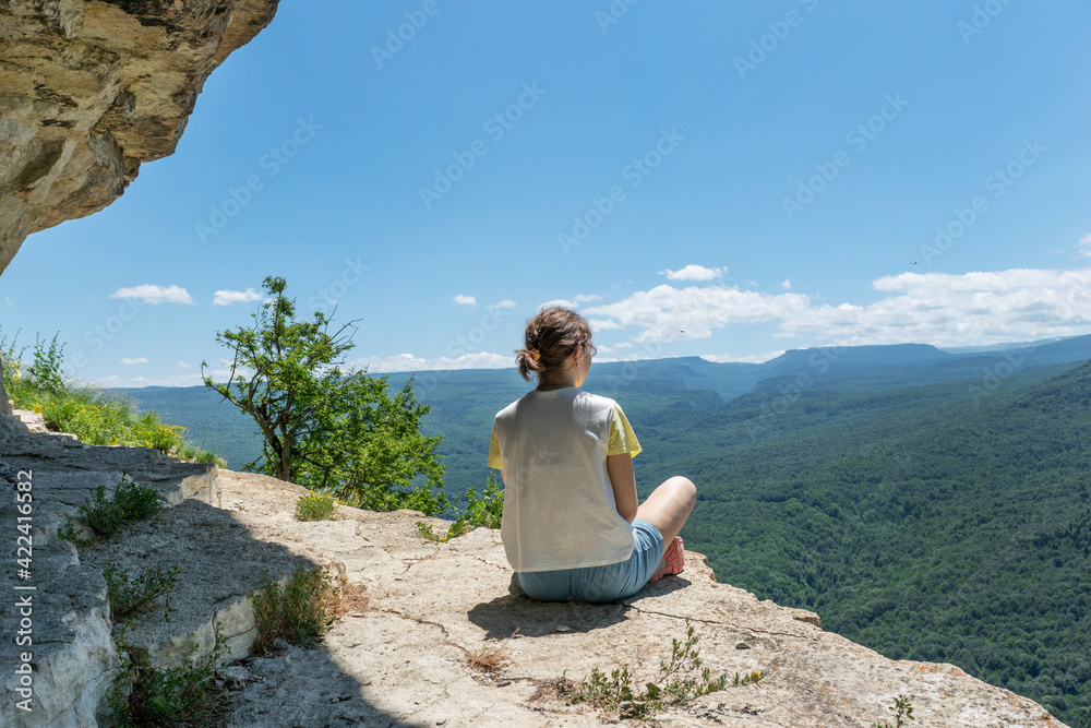 Young female sit on cliff on peak in high mountains looking over green mountains with feeling of relexation. Healthy lifestyle, adventure during hiking in mountains.