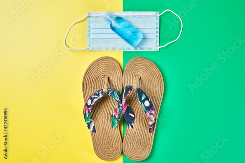 Studio photo, summer sandals full size on two colors yellow and green vertical background, antiseptic gel and face mask ready for holidays