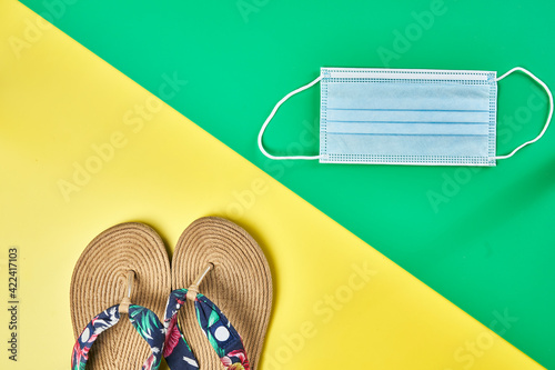 Studio photo, diagonal summer sandals on two colors yellow and green vertical background and face mask ready for holidays