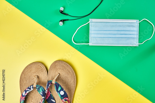 Studio photo, diagonal summer sandals on two colors yellow and green vertical background, headphones and face mask ready for holidays
