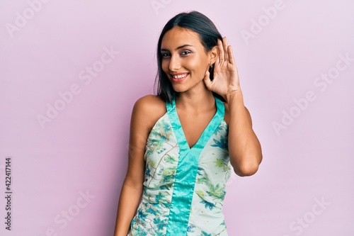 Young brunette woman wearing elegant summer shirt smiling with hand over ear listening and hearing to rumor or gossip. deafness concept.