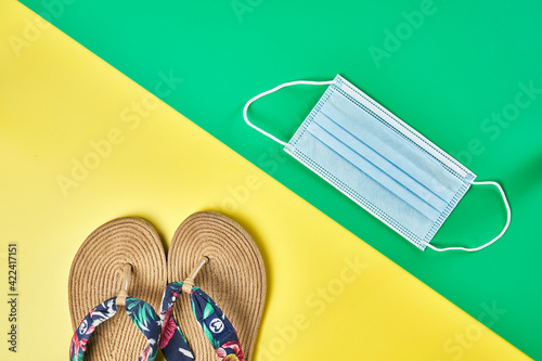 Studio photo, diagonal summer sandals on two colors yellow and green vertical background and lateral face mask ready for holidays