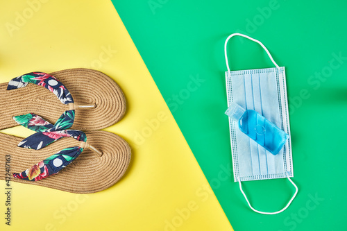 Studio photo, lateral view summer sandals on two colors yellow and green vertical background, antiseptic gel and face mask ready for holidays