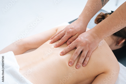 Top close-up view of male masseur massaging back and shoulder blades of female lying on massage table at spa salon. Beautiful young woman with perfect skin getting relaxing massage.