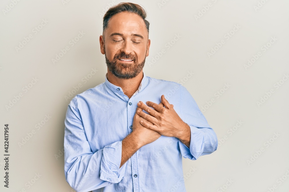 Handsome middle age man wearing business clothes smiling with hands on chest, eyes closed with grateful gesture on face. health concept. Handsome middle age man wearing business clothes smiling with hands on chest, eyes closed with grateful gesture on face. health concept.