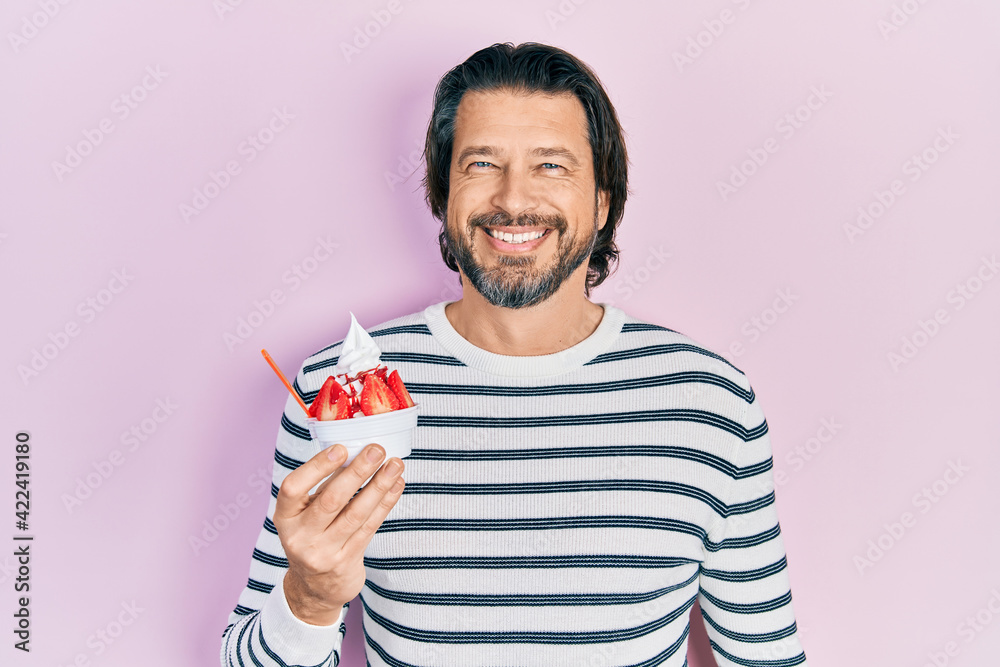 Middle age caucasian man eating strawberry ice cream looking positive and happy standing and smiling with a confident smile showing teeth Middle age caucasian man eating strawberry ice cream looking positive and happy standing and smiling with a confident smile showing teeth