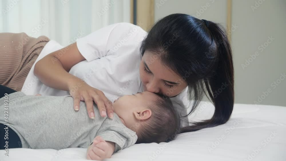 Closeup young asian mother kiss little baby girl with sleep and innocence on bed in bedroom at home, mom care newborn and bonding, woman feeling happiness with daughter, family and lifestyle concept. Closeup young asian mother kiss little baby girl with sleep and innocence on bed in bedroom at home, mom care newborn and bonding, woman feeling happiness with daughter, family and lifestyle concept.