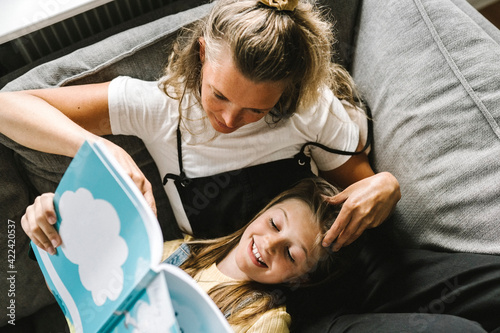 Daughter reading book with mother in living room