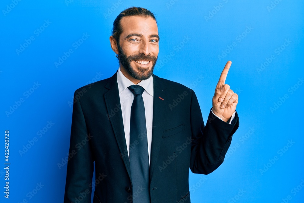 Attractive man with long hair and beard wearing business suit and tie smiling happy pointing with hand and finger to the side Attractive man with long hair and beard wearing business suit and tie smiling happy pointing with hand and finger to the side