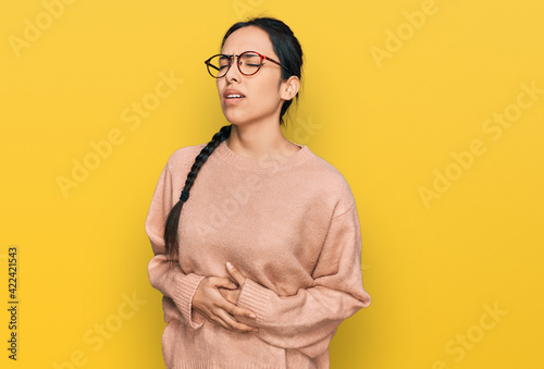 Young hispanic girl wearing casual clothes and glasses with hand on stomach because nausea, painful disease feeling unwell. ache concept. © Krakenimages.com