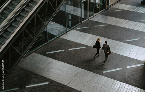 Rear view of male and female colleagues walking by escalator on walkway