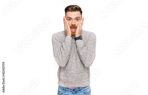 Young redhead man wearing casual winter sweater afraid and shocked, surprise and amazed expression with hands on face