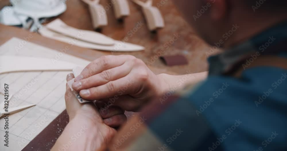 Male caucasian carpenter sanding wooden bird toy with sandpaper on work table at workplace. Worker man working with craft toy wing detail made of wood, polish surface. Manufacturing and hobby concept Male caucasian carpenter sanding wooden bird toy with sandpaper on work table at workplace. Worker man working with craft toy wing detail made of wood, polish surface. Manufacturing and hobby concept
