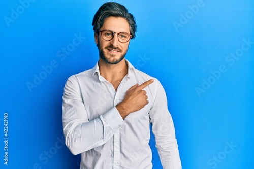 Young hispanic man wearing casual clothes and glasses smiling cheerful pointing with hand and finger up to the side