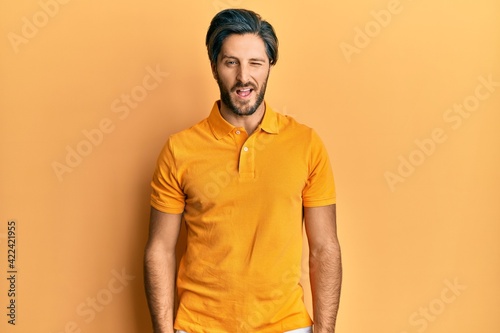 Young hispanic man wearing casual yellow t shirt winking looking at the camera with sexy expression, cheerful and happy face.