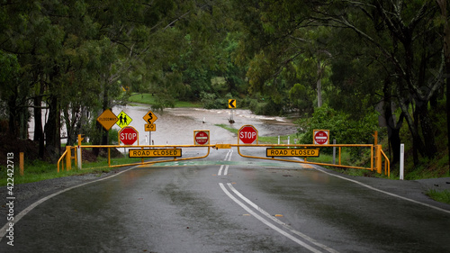 Bright Yellow and Red Stop signs warning motorists that the road is closed and flooded. Youngs Crossing, Petrie, Queensland, Australia.