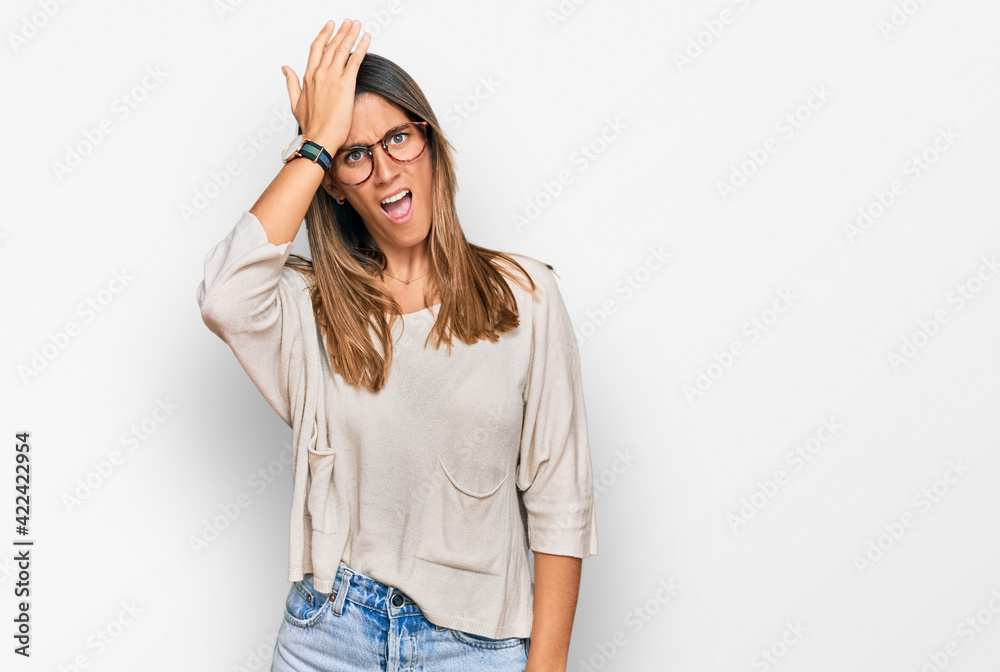 Young woman wearing casual clothes and glasses surprised with hand on head for mistake, remember error. forgot, bad memory concept.