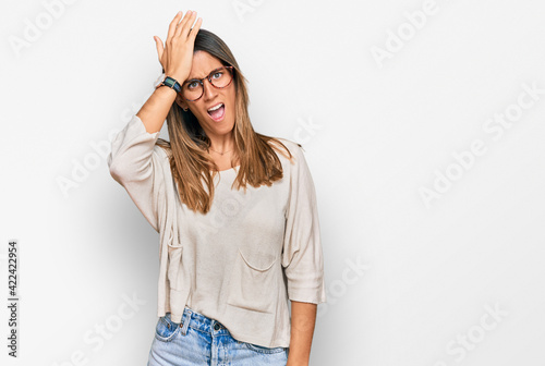 Young woman wearing casual clothes and glasses surprised with hand on head for mistake, remember error. forgot, bad memory concept.