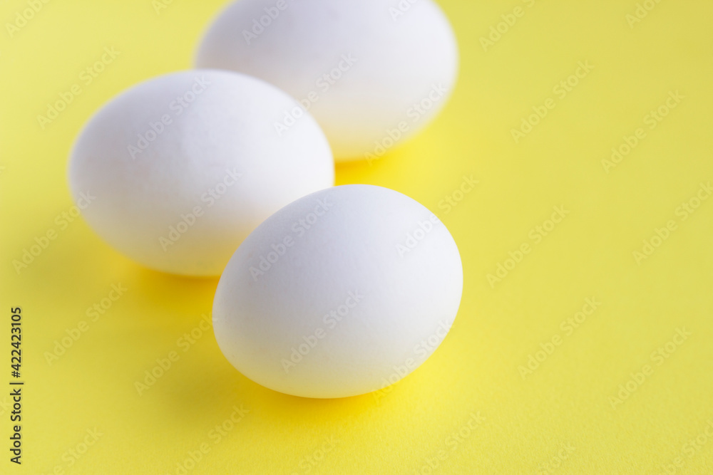 Three white eggs on yellow background. Happy Easter. Fresh eggs for breakfast. Spring color and forms. Organic food for healthy lifestyle. Three white eggs on yellow background. Happy Easter. Fresh eggs for breakfast. Spring color and forms. Organic food for healthy lifestyle.