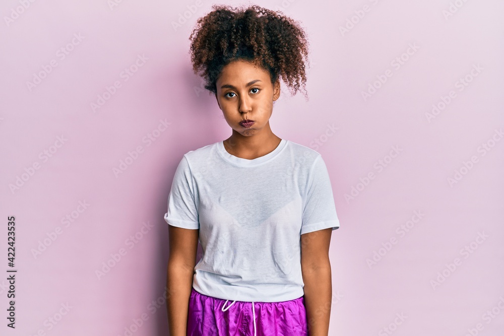 Beautiful african american woman with afro hair wearing sportswear puffing cheeks with funny face. mouth inflated with air, crazy expression. Beautiful african american woman with afro hair wearing sportswear puffing cheeks with funny face. mouth inflated with air, crazy expression.