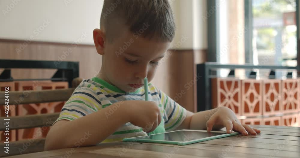 A portrait of a child sits at a table at home and draws on his tablet with a special pen, a preschooler uses a special tablet for drawing. A portrait of a child sits at a table at home and draws on his tablet with a special pen, a preschooler uses a special tablet for drawing.