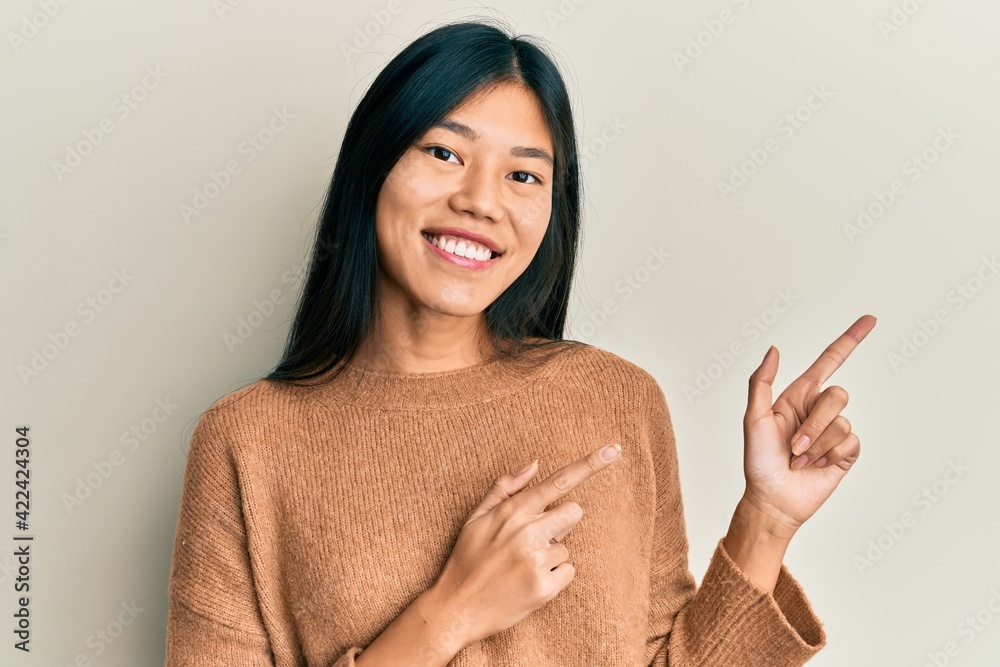 Young chinese woman wearing casual clothes smiling and looking at the camera pointing with two hands and fingers to the side. Young chinese woman wearing casual clothes smiling and looking at the camera pointing with two hands and fingers to the side.