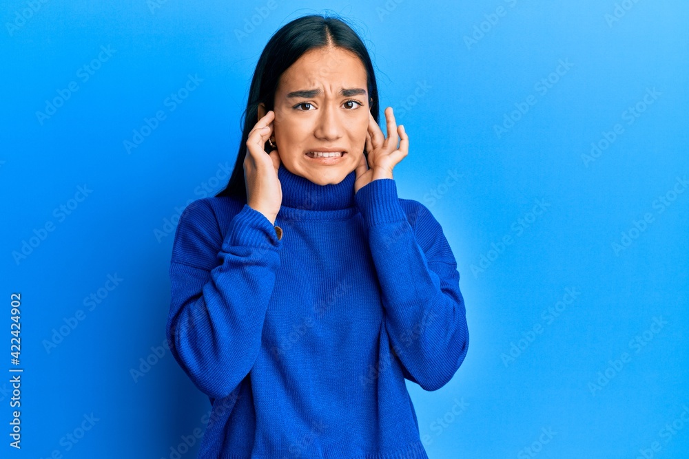 Young asian woman wearing casual winter sweater covering ears with fingers with annoyed expression for the noise of loud music. deaf concept. Young asian woman wearing casual winter sweater covering ears with fingers with annoyed expression for the noise of loud music. deaf concept.