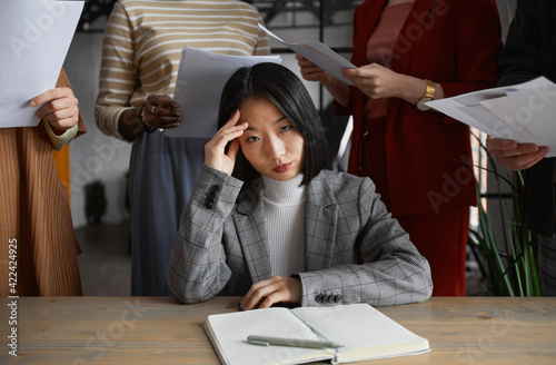 Bild auf Leinwand Portrait of annoyed Asian businesswoman looking at camera surrounded by group of
