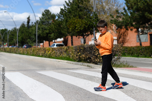 Child looks at a cell phone while crossing a crosswalk on a roadway