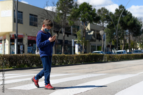 Child looks at a cell phone while crossing a crosswalk on a roadway