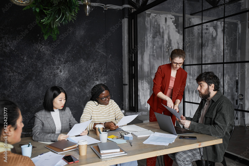 Diverse business team discussing project in black office interior focus on young businesswoman wearing red jacket, copy space Diverse business team discussing project in black office interior focus on young businesswoman wearing red jacket, copy space