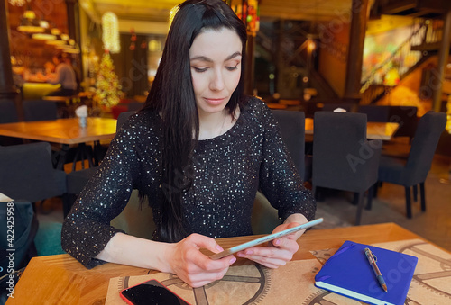 A girl with dark hair is working in a cafe with a tablet, a phone and a notebook are nearby. Coworking, workflow organization. Business concept.