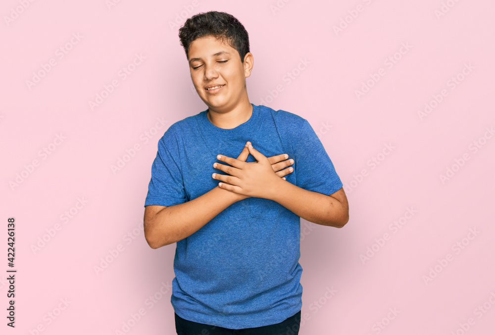 Teenager hispanic boy wearing casual clothes smiling with hands on chest with closed eyes and grateful gesture on face. health concept. Teenager hispanic boy wearing casual clothes smiling with hands on chest with closed eyes and grateful gesture on face. health concept.