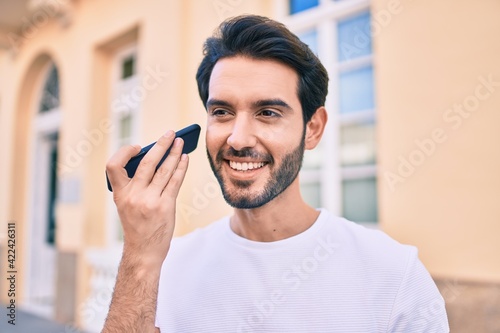 Young hispanic man smiling happy listening audio message using smartphone at city.