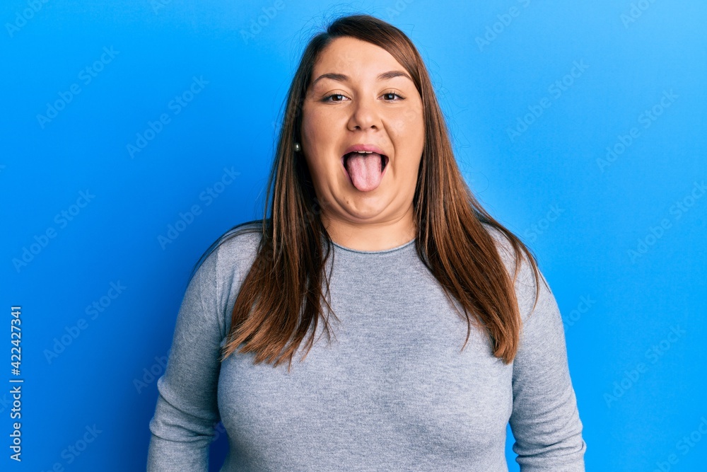 Beautiful brunette plus size woman wearing casual clothes sticking tongue out happy with funny expression. emotion concept. Beautiful brunette plus size woman wearing casual clothes sticking tongue out happy with funny expression. emotion concept.